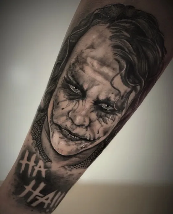 Porträt des Jokers mit verschmierter Schminke und Schriftzug Ha Ha als Armtattoo